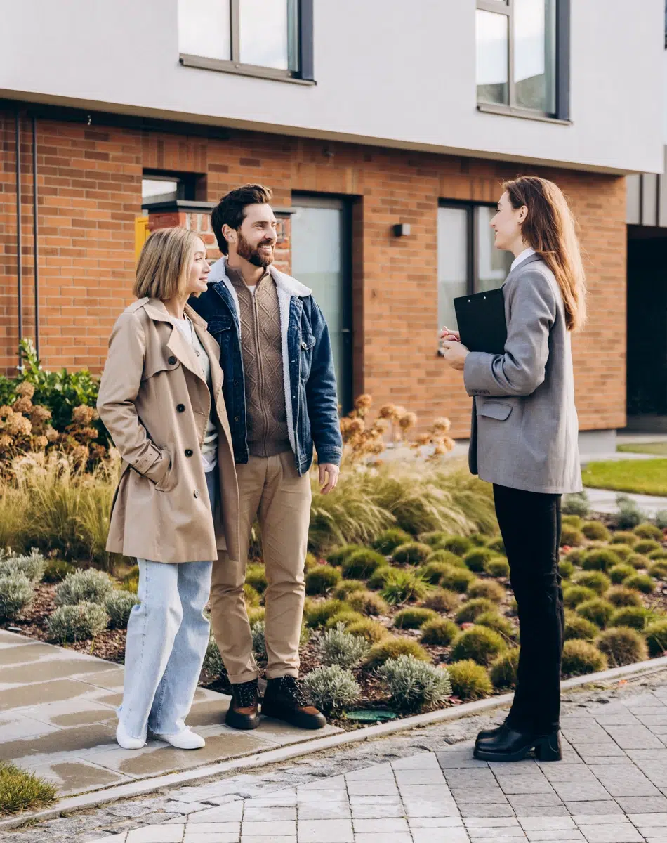 Couple discutant avec un agent immobilier devant une maison.